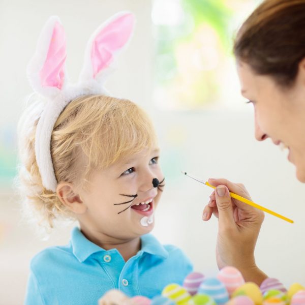 Mother and kids color Easter eggs. Face painting for little child. Little boy with bunny ears and mom dye eggs. Easter egg hunt. Family celebration and home decoration for spring holiday.